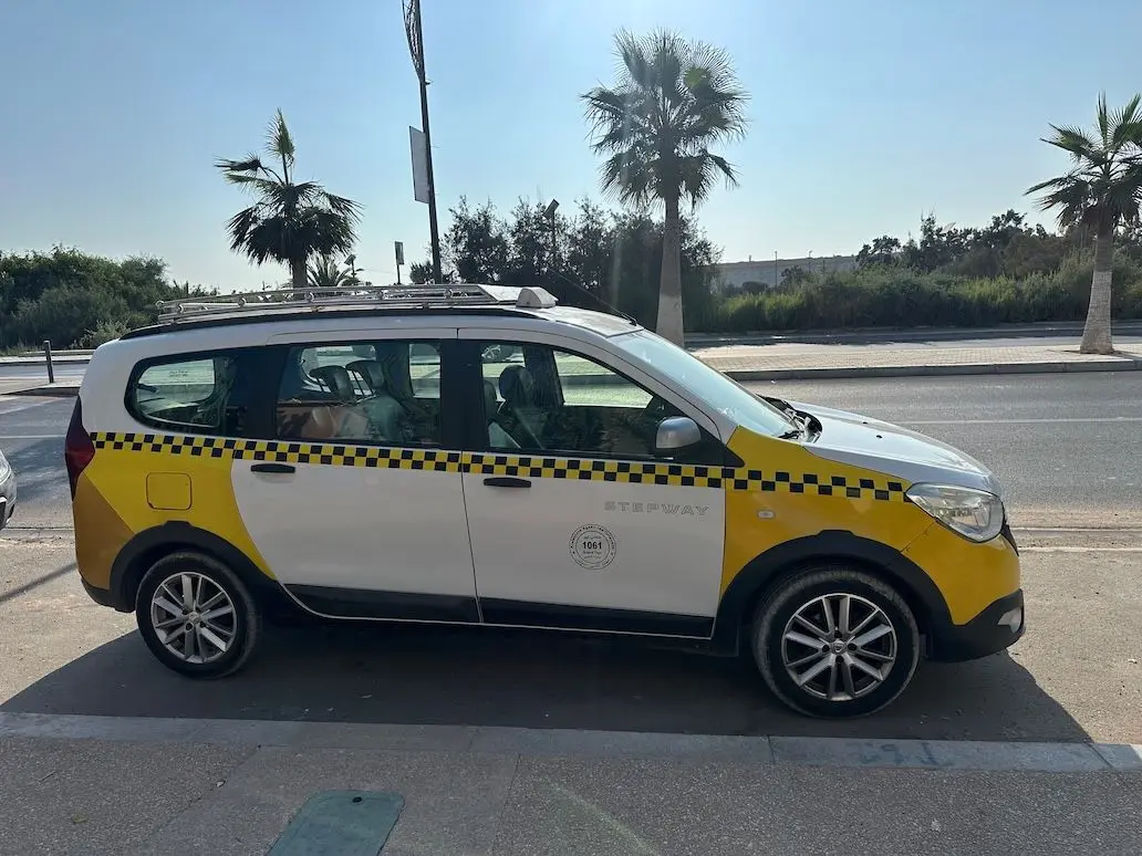 A white and yellow Moroccan grand taxi parked at the roadside