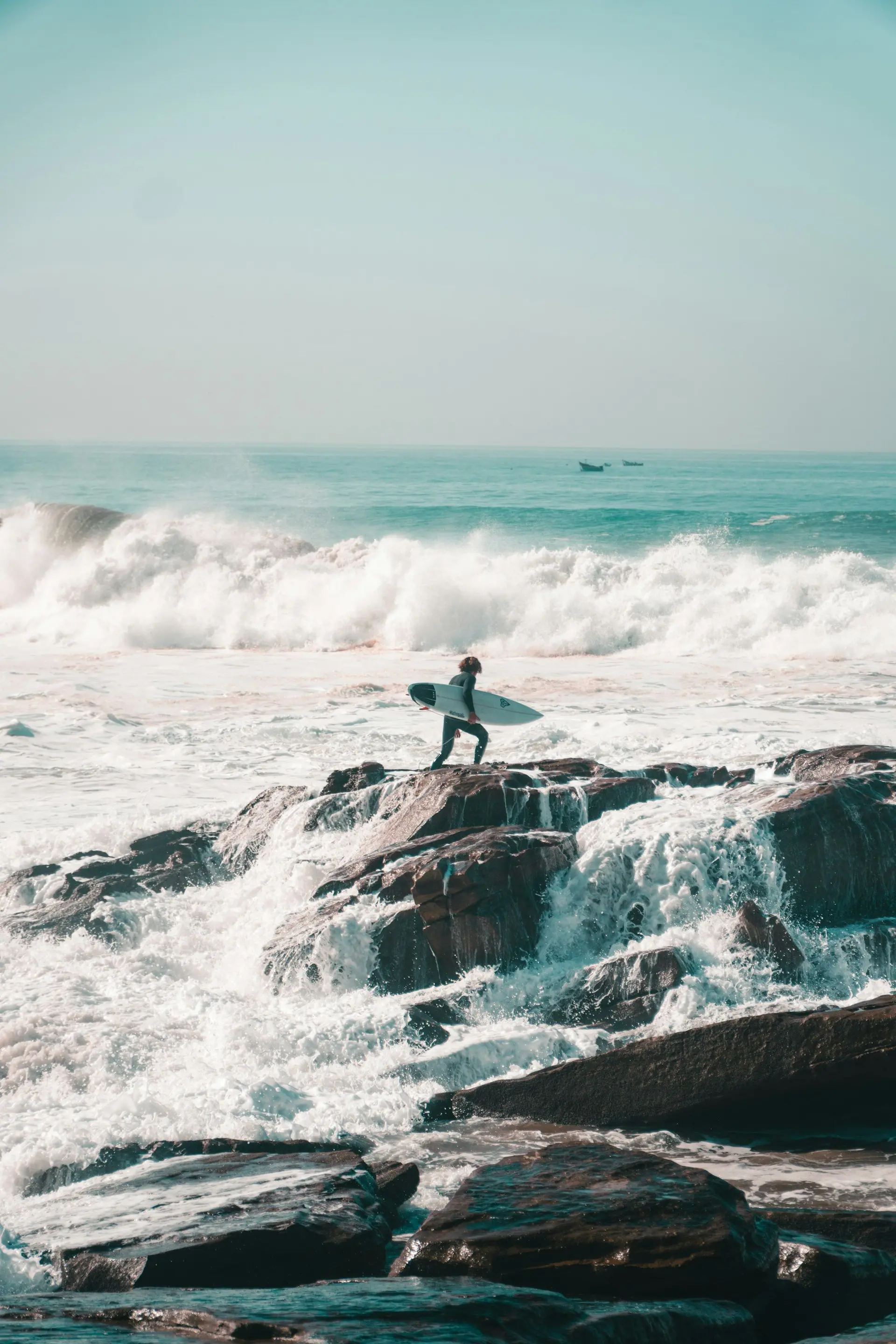 Surfer in a wetsuit crossing the rocks to the waves in Taghazout